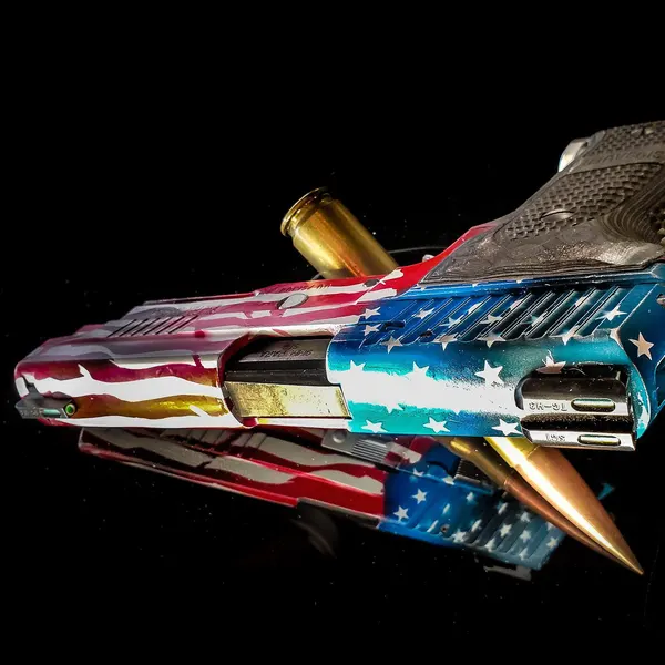 1911 pistol with a distressed American flag Cerakote finish on a black reflective surface.