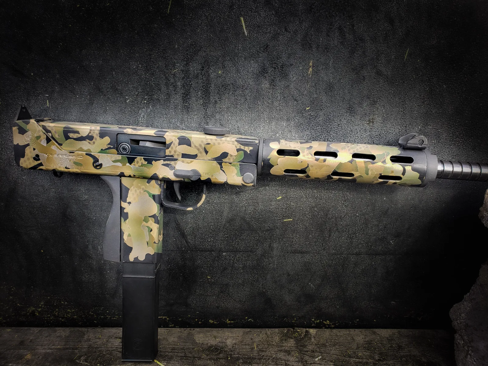 Side-folding 9mm carbine finished in multicam-pattern Cerakote against a dark background.
