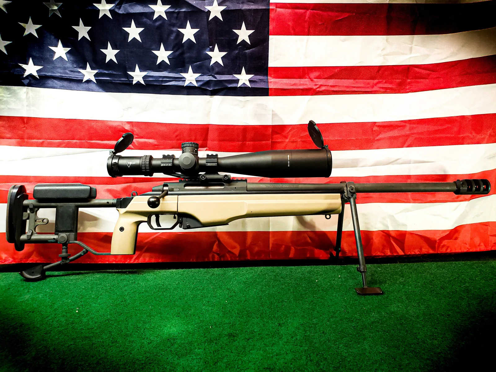 Bolt-action precision rifle with a flat dark earth Cerakote stock and black barrel in front of an American flag.