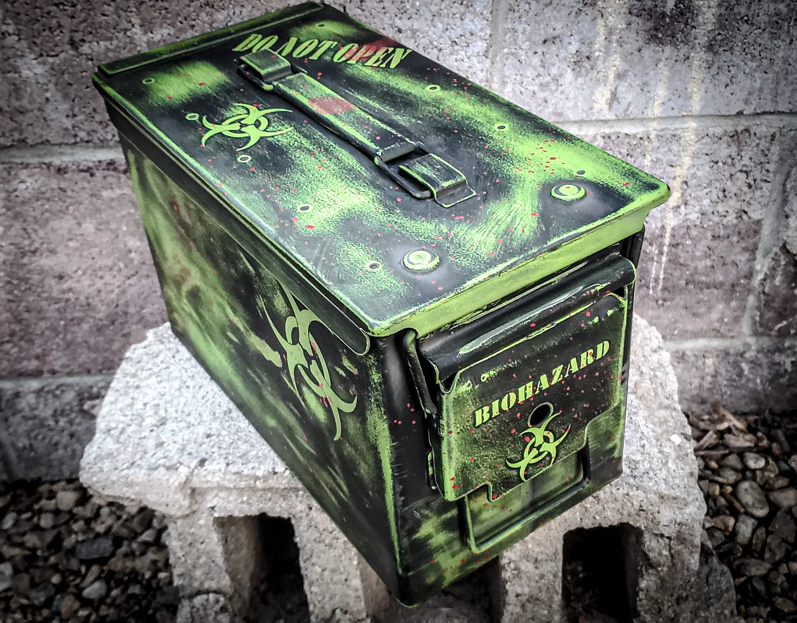 Steel ammo can coated in distressed green and black Cerakote with biohazard symbols and stencil lettering.